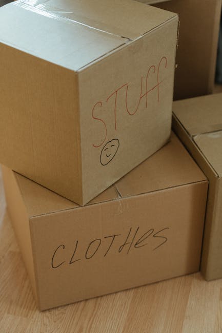 Close-up view of three cardboard moving boxes placed on a light wooden floor inside a residential property. The top box has the word 'STUFF' written in red marker on its side, along with a small smile