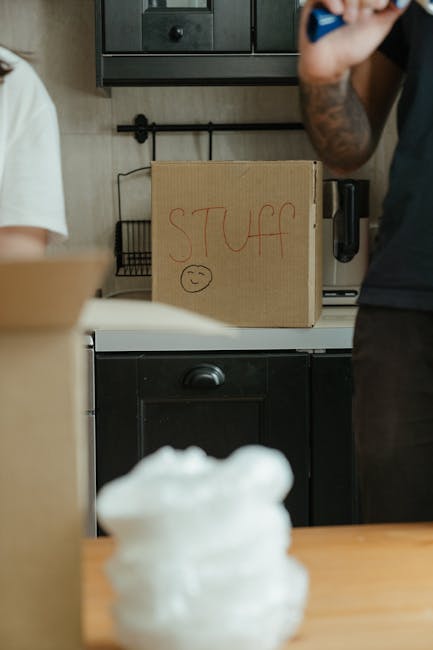 Close-up view of three cardboard moving boxes placed on a light wooden floor inside a residential property. The top box has the word 'STUFF' written in red marker on its side, along with a small smile
